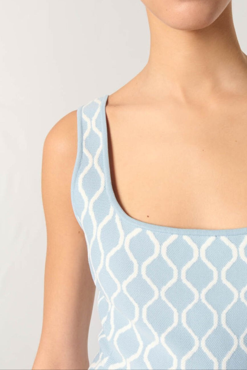 Woman wearing a light blue sleeveless top with a geometric pattern on a plain background