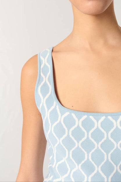 Woman wearing a light blue sleeveless top with a geometric pattern on a plain background
