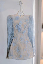 Light blue lace dress on a hanger against a white wall with a handbag and shoes in the background.